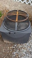 Top view of the firepit with metal mesh fire screen in place, showing circular safety cover and square base.