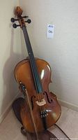 Full view of cello standing with soft case on floor against wall