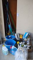 Various cleaning supplies organized on the floor in front of a wall and cleaning tools stored in a corner