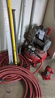 Porter Cable Jet Stream air compressor with attached gauges and a coil of red air hose, yellow expandable pole tool, and 48-inch steel ruler alongside several long tools.