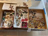 Three cardboard trays with mixed costume jewelry include various brooches, earrings, pendants and charms