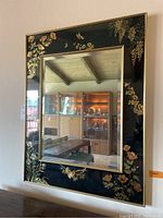Full front view of the framed mirror showing the reflective glass and black frame with gold floral and butterfly decorations.