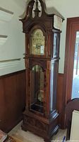Angled full view of tall grandfather clock showing wood cabinet and bonnet.