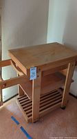 Full view of natural wood kitchen cart with butcher block top and two storage shelves below, on wheels.