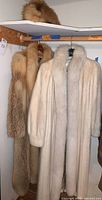 Small tan-red fox fur pillbox hat on shelf above two fur coats