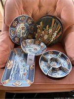 Various Oriental style ceramic serving dishes including rectangular tray, round plates, divided dish, and two-tiered bowls placed on chair.