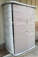 Full view of the closed Rubbermaid buff-colored storage shed showing two doors and slightly warped plastic structure.