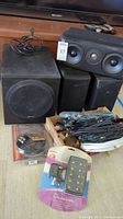 Polk Audio powered subwoofer and three speakers with box of cables and accessories shown together on floor.