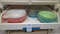 All six bowls displayed in cabinet drawer: three pink Gooseberry bowls left, clear turquoise/gold patterned bowl back center, green and blue bowls right front