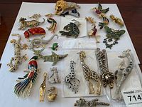 Overhead view of entire lot showing 16 animal and bird brooches and a set of giraffe earrings on white background