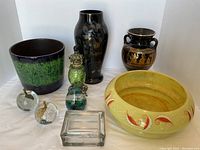 Full lot view showing black vase, ceramic jardiniere, Greek-style vase, yellow glass bowl, paperweights, perfume bottles, and glass dish