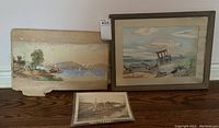 Photo of both watercolour paintings and black and white warship photograph displayed together on a wooden surface