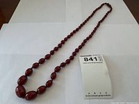 Full-length view of the cherry amber Bakelite necklace laid flat beside a lot tag
