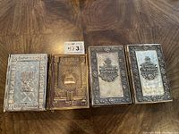 Top view of the 4 prayer books showing ornate metal covers with menorahs, Hebrew text, and embossed designs in silver and bronze tones.