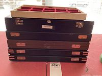 Stack of six closed jewelry ring boxes with a beige and red velvet interior tray placed on top, showing metal latches and slight wear.