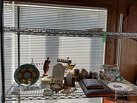 Overview of Judaica items on a metal shelf with decorative seder plate, menorahs, figurines, plates, and religious book.
