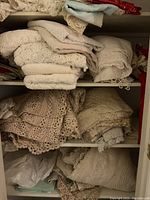 Overview of three shelves filled with folded lace and crocheted linens