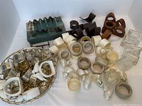 Overview of lots including napkin rings in wood, plastic, mother-of-pearl, and metal placed in basket and spread out, along with utensil rests.