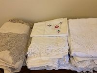 Three stacks of folded vintage tablecloths showing crocheted lace, cutwork, and cross-stitch pieces