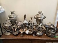 Front view of entire lot on wooden cabinet showing samovars, trays, teapot, bowls and candelabra