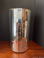 Front view of the cylindrical mirrored waste basket/pedestal showing vertical mirrored panels and gold edges