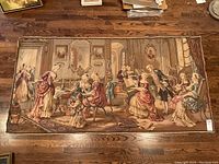 Full view of the tapestry laid on wooden floor showing multiple figures in a detailed 18th-century style parlor scene.