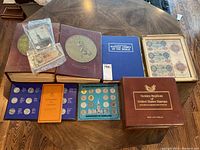 Overview of all albums, boxes, coin and medallion sets, postcards and framed display laid out on table