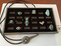 Overview of bolo tie slide, cord and seven turquoise rings in tray