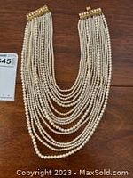 Full view of 15 strands of faux pearls with gold-tone clasp, showing length and layering