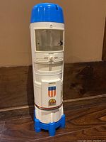 Front view of vintage Six Million Dollar Man rocket ship toy showing clear window compartment, logos, and overall white and blue color scheme.