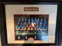 Frontal photo of the framed 2006 Italy World Cup champion team photograph showing the team in blue kits, ivory mat with plaque and flags.