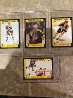 Four Bobby Orr hockey cards in yellow and black bordered cards, each in clear plastic screw down holders, placed on a tiled floor.