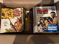 Box of vintage War Picture Library graphic novels from the 1960s-1970s showing covers with war scenes, soldiers, tanks, and weapons.