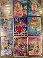 Photo of all 9 DVDs showing eight Barbie movies and one My Little Pony DVD, colorful covers with Barbie in fantasy themes.