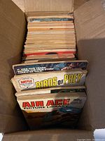 Top view of a box filled with about 40 vintage war comics showing colorful spines and partially visible covers.