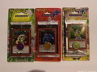Three MetaZoo collectible card game blister packs side by side. Each pack includes a promo card visible through the packaging and a metallic coin.