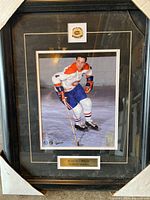 Framed photo of Hall of Famer Jean Beliveau with Montreal Canadiens hockey uniform and team emblem, nameplate included, showing corner damage.