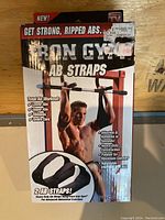 Front view of the box packaging showing the Iron Gym Ab Straps branding, features, and an image of a man demonstrating use on a pull up bar.