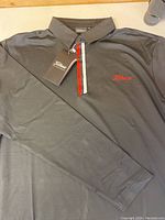 Front view of black long sleeve Titleist golf shirt, showing collar, left arm, embroidered red Titleist logo, and tags attached.