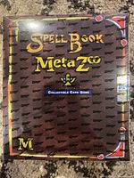 Front view of sealed MetaZoo Spell Book showing brown cover with yellow title text and decorative corners.