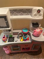 Full view of the children's play kitchen showing stove, oven, sink, microwave, and pink teapot and kettle accessories on countertop.
