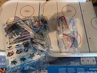 Foldable hockey rink playboard with two red goal nets and multiple sealed accessory bags containing figures, hockey sticks, and NHL team stickers.
