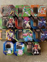 Photo showing 12 Pokemon opened metal tins with various Pokemon character artwork and transparent windows on lids.