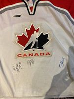 Front view of the white Team Canada women's hockey jersey showing the maple leaf logo and three signatures including Geraldine Heaney and Cassie Campbell.