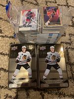 Two tins of 2023-24 Upper Deck Series Two Hockey Cards with Chicago Blackhawks player images, placed on carpet.