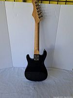 Back view of black BC electric guitar showing solid body, bolt on maple neck, tuning pegs, six strings but missing two strings overall.