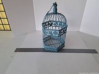 Full view of blue metal birdcage with hexagonal base and top hanging hook