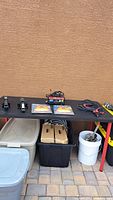 Overview photo showing two car jacks, hazard lights, battery charger, and jumper cables on black table