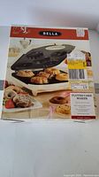 Front view of the Bella Fluted Cake Maker in original box with pictures showing finished cakes and donuts.