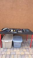 Wide view showing all tools on black table with tubs underneath. Tools include pulley, pliers, hammer, cutters, and other small hand tools.